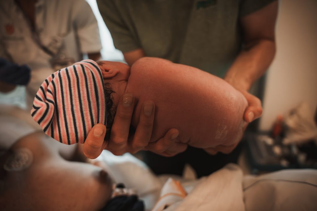 Newborn baby in a striped hat held by her mother, birth at the AMC Amsterdam with doula support