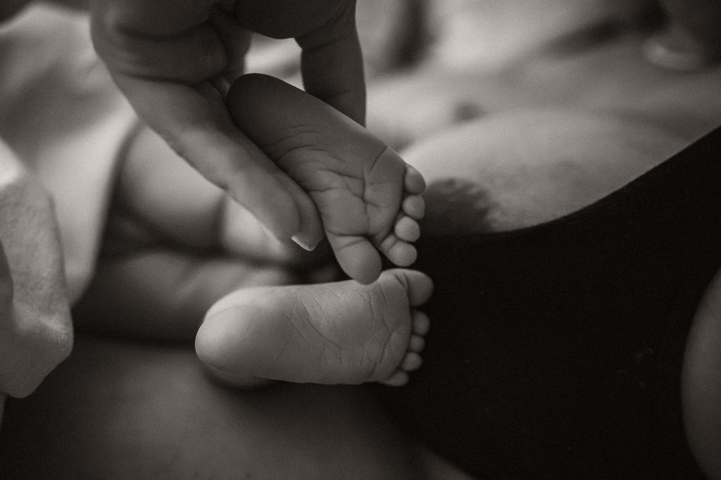 Newborn feet in her parents' hands, black and white, doula support at a hospital birth in Arnhem